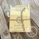 Handmade goat's milk soap bar with a loofah on a wooden surface, branded 'The Rusty Sapphire'.
